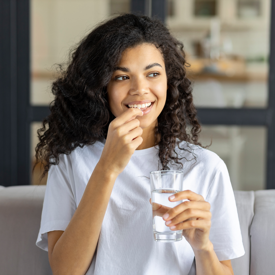 Woman holding a glass of water tablet and smiling indoors