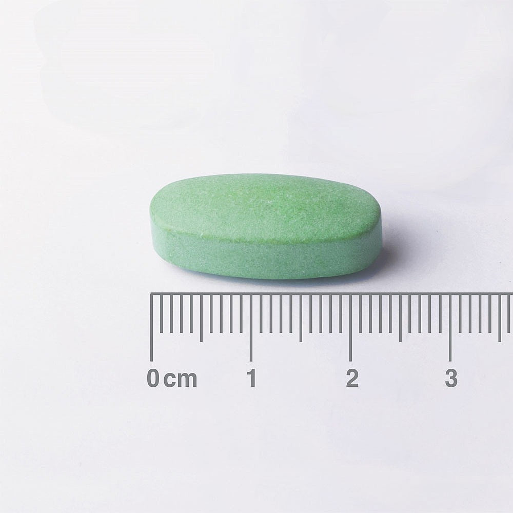Green pill with a ruler for scale on a white background