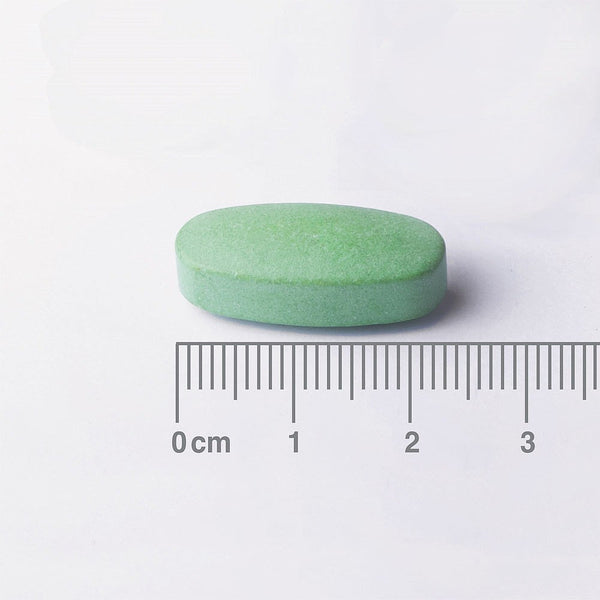 Green pill with a ruler for scale on a white background