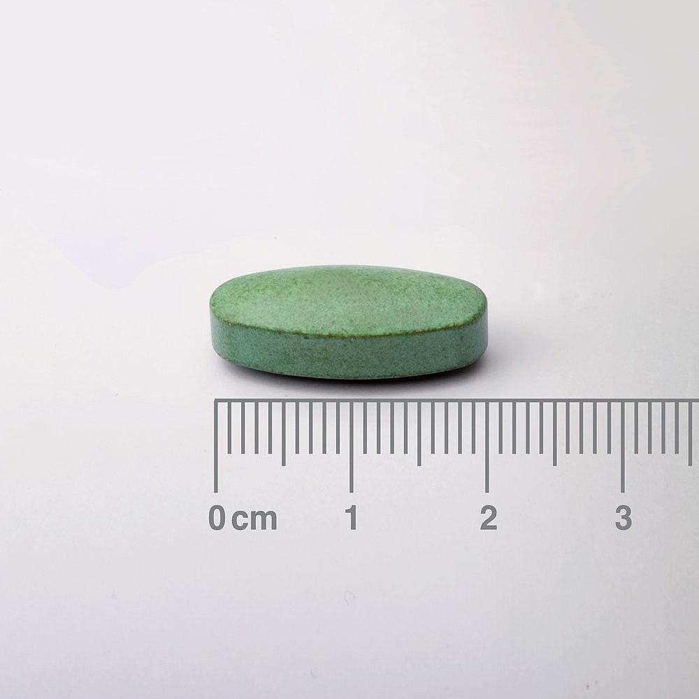 Green pill with a ruler for scale on a white background