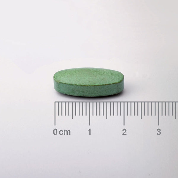Green pill with a ruler for scale on a white background