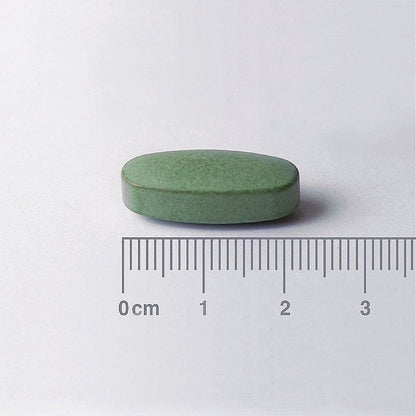Green pill with a ruler for scale on a white background