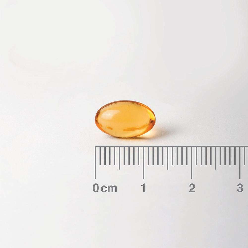 Amber-colored supplement capsule with a ruler for scale on a white background