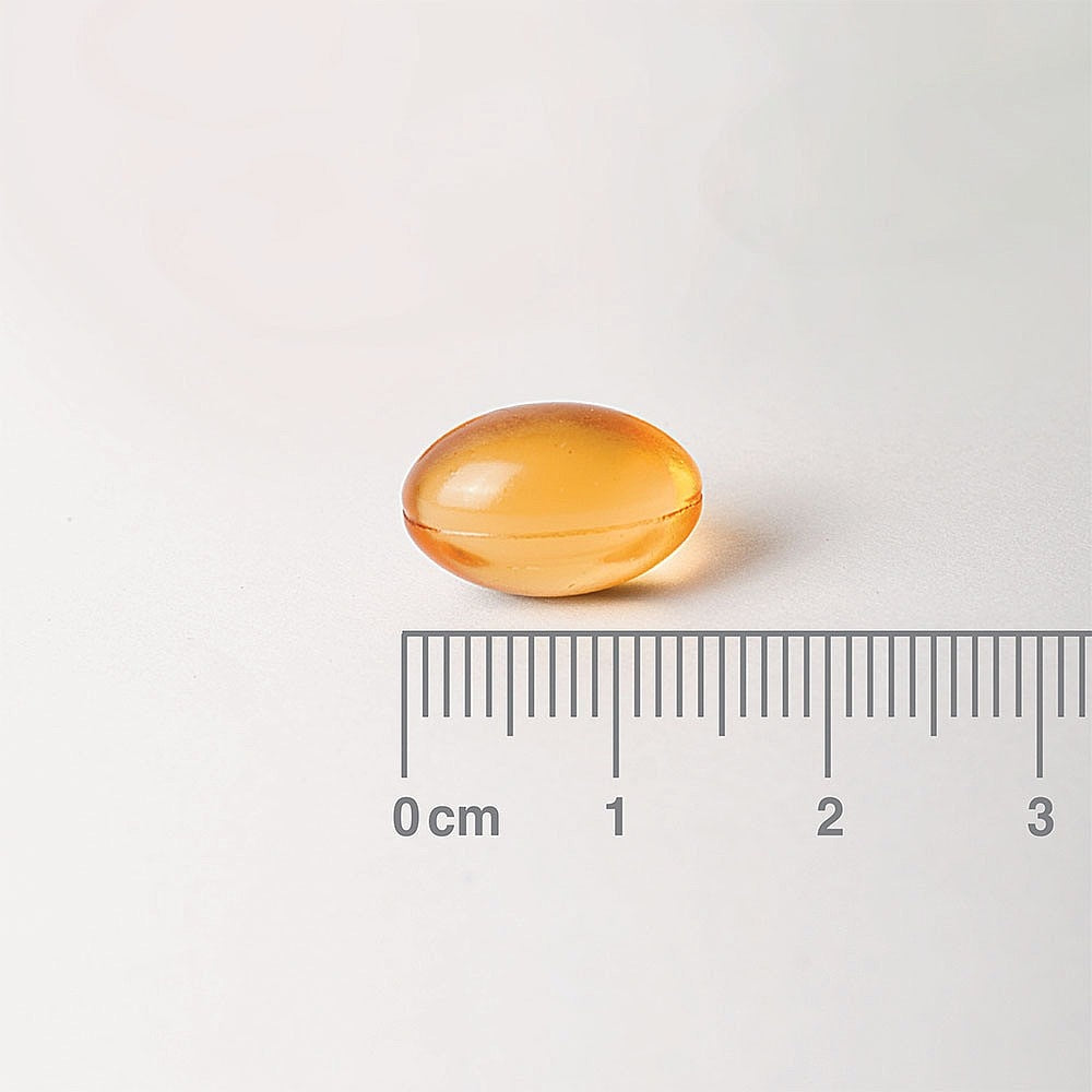 Yellow capsule pill on a white background with a ruler for scale.