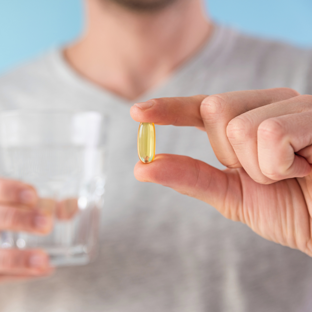 Person holding a yellow supplement capsule with a blurred background