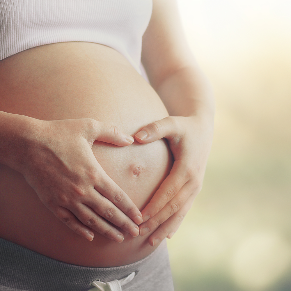 Close-up of a pregnant belly with hands gently touching it against a blurred background