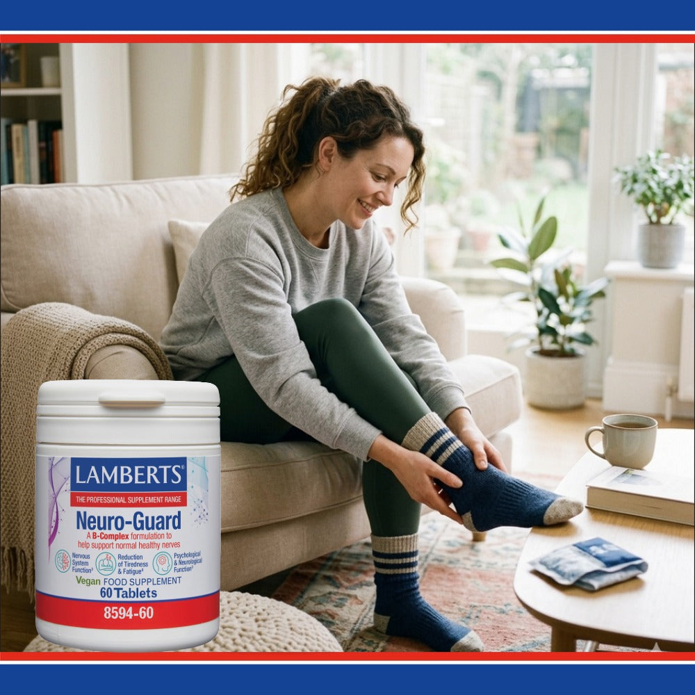 A woman sitting on a beige couch in a bright living room is putting on a blue striped sock while holding a large white tub of Lambert's Neuro-Guard supplement in the foreground.