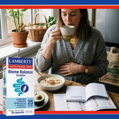 Woman drinking from a mug with a box of Lamlerts Biome Balance Sensitive supplement in the foreground.