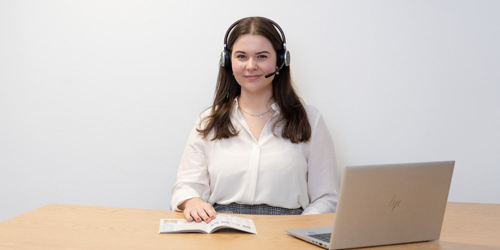 Person wearing a headset sitting at a desk with a laptop and notebook.